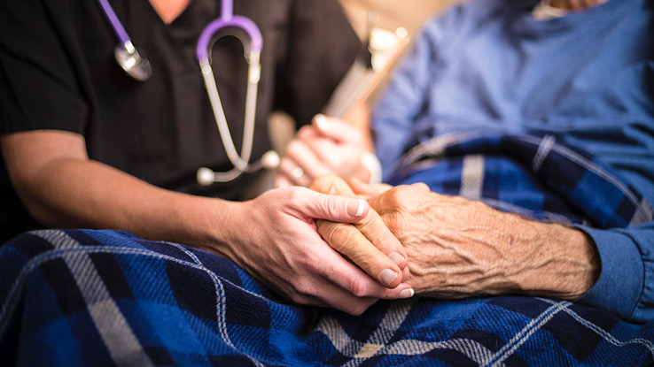 Caregiver holding the hands of someone with late stage dementia